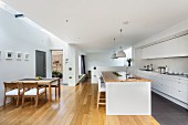 Offene Deisgnerküche - Essplatz mit Holz Tischgarnitur, gegenüber Küchenblock und weisser Einbauküche