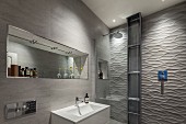 Designer bathroom - washbasin against tiled wall, mirror in niche, shower area with 3D structured tiles on wall