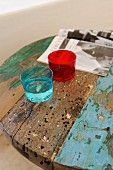 Colourful drinking glasses on round, vintage table made from recycled wood