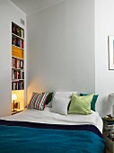 Scatter cushions on double next to bookcase in niche and bedside lamp