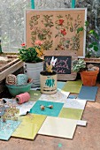 Alte Blechdosen und Blumentöpfe mit Pflanzen, Garnrollen, etc. auf Arbeitsfläche aus Fliesen-Patchwork