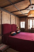 Doppelbett in Dunkelrot mit passenden Zierkissen; Wandvertäfelung mit schmalen Lisenen und bemalten Bordüren