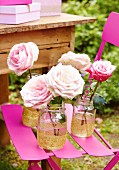 Rosafarbene Rosen in vergoldeten Gläsern auf pinkfarbenem Gartenstuhl