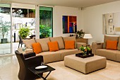 Elegant, beige sofa set with orange scatter cushions and brown leather armchair in front of terrace doors