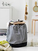 A wooden stool with a homemade, black-and-white striped fabric bag as a laundry basket in a modern bathroom