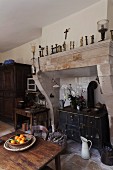 Rustic, French kitchen with antique wood-burning cooker in deep former fireplace and bowl of oranges on wooden table