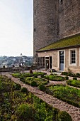Terrace garden with geometric beds adjoining house built against historical tower facade