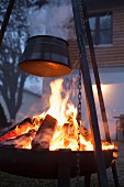 Metallgestell mit Kochtopf über brennender Feuerschale in der Abenddämmerung