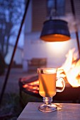Hot drink in glass mug in front of fire in brazier in garden