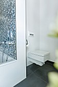 A square modern toilet installed discreetly in a corner behind the bathtub