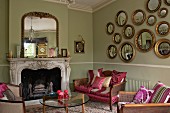 Gallery of gilt-framed, convex mirrors in interior with antique, re-upholstered seating, 60s glass table and historical fire surround