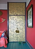 Elegant Chinese pattern in gold on doors of wardrobe contrasting with raspberry walls and petrol-blue floor
