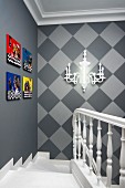 Head of staircase on elegant lantern with brightly coloured pictures and sconce lamp on walls in shades of grey