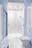 Pedestal toilet against wall painted pale blue in front of white, floor-level shower