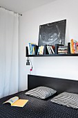 Black bookshelf above double bed with black and white patterned textiles in bedroom