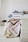 Spitzen-Patchworkdecke und weiße Vintage-Truhe am Fussende eines Bettes