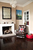 Brown leather armchair next to open fireplace in corner of room painted pale brown with dark wooden floor