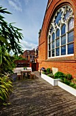 Furnished wooden deck with raised beds adjoining brick facade of Neogothic church