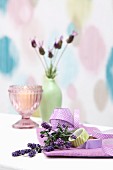 Sprigs of lavender, ribbon and washi tape in front of candle and vase of lavender