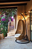Wicker hanging chair on Mediterranean terrace covered in bougainvillea