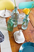 Flowers in retro glass bottles and crockery on wooden table