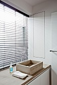 In eine Betonplatte integriertes Waschbecken vor Badfenster mit Jalousie