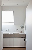White bathroom with concrete sinks and white base cabinets lit by skylight