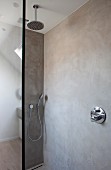 Regenbrause und Handbrause in begehbarer Dusche mit marmorierten Betonwänden und Glastrennwand