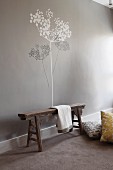 Rustic wooden bench against pale grey wall with tree mural in grey and white