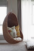 Comfortable wicker hanging chair in interior with walls painted pale grey