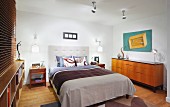 Double bed with upholstered headboard next to fifties-style sideboard in modern bedroom