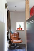 Brauner Ledersessel in Zimmerecke mit Retro Tischleuchte vor Fenster