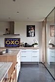 Open-plan kitchen with modern, white kitchen counter and blue. vintage advertising sign in renovated country house belonging to artist