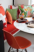 Orangefarbener Klassikerstuhl vor Tisch mit Marmorplatte, seitlich drapierte Kissen auf Sitzbank