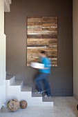 Concrete staircase and modern artwork on brown wall in hallway; man walking up stairs