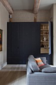 Fitted cupboard with board front in niche and grey sofa in foreground