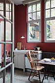 View through open lattice doors of wooden armchair with high backrest at dining table in simple kitchen with walls painted Bordeaux red