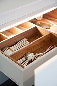Open cutlery drawer with exotic wooden compartments, silver cutlery and integrated lighting
