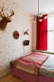 Simple double bed with striped blanket and stylised hunting trophies and TV on wall with floral wallpaper
