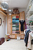 Dressing room with women's clothing on clothes rack below shelves and old wooden wardrobe in background