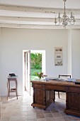 Antique desk in simple room with terracotta floor and white, wood-beamed ceiling