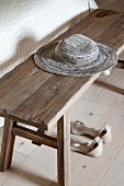 Lady's sandals on floor under sun hat on rustic wooden bench