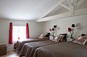 Mehrere Einzelbetten mit brauner Tagesdecke, dazwischen Nachtkästchen und Tischleuchten mit roten, kleinen Schirmen, im Dachzimmer mit weisser Holzkonstruktion