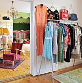 Retro women's clothing hanging on clothes rack next to open door with view into feminine bedroom