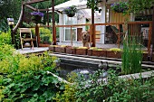 Dog on terrace with rectangular wooden planters next to pond and herbaceous border in foreground