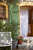 Granite steps, a bench and an olive tree in front of a door with shutters and a curtain in a French country house