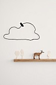 Deer figurine and cut-out paper trees on narrow floating shelf below hand-crafted wire cloud stuck to wall with washi tape