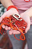 Red and orange bead necklaces held in woman's hands