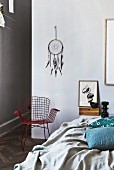 Hand-crafted dreamcatcher above wire armchair; bed with throw and scatter cushions in foreground