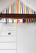 White ladder leading to gallery in attic with colourful ribbon curtain screening entrance